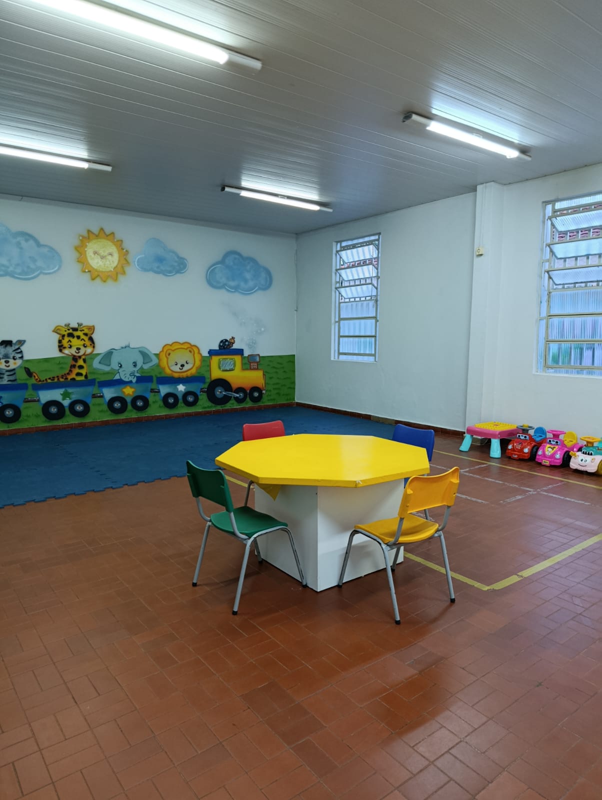 Sala com mesa redonda amarela e parede decorada com trenzinho